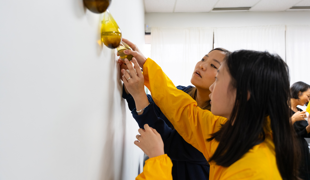 Community liaison Nicole Kang Ahn helping a young girl rehang a tear-shaped glass vessel after filling it with creek water
