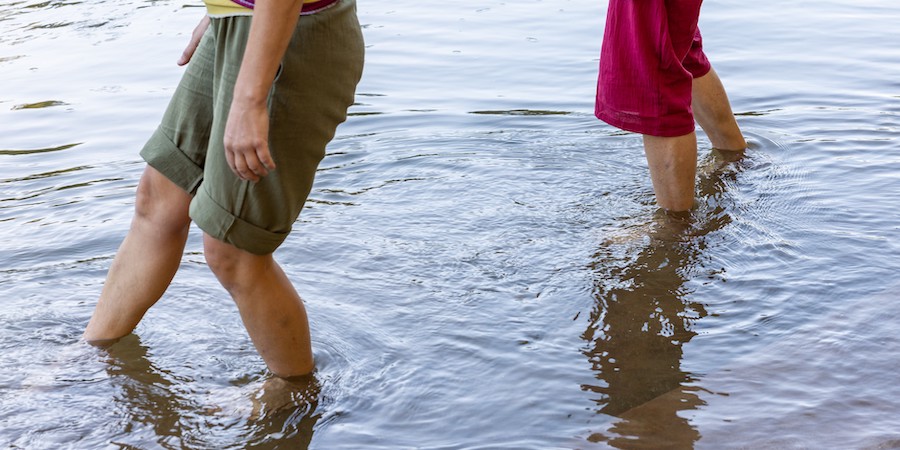 Legs of two dancers walking with their feet submerged in the water. Photo by John Ramspott